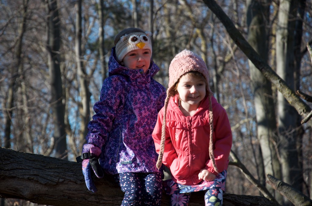 Two girls sitting on a log in the woods. 